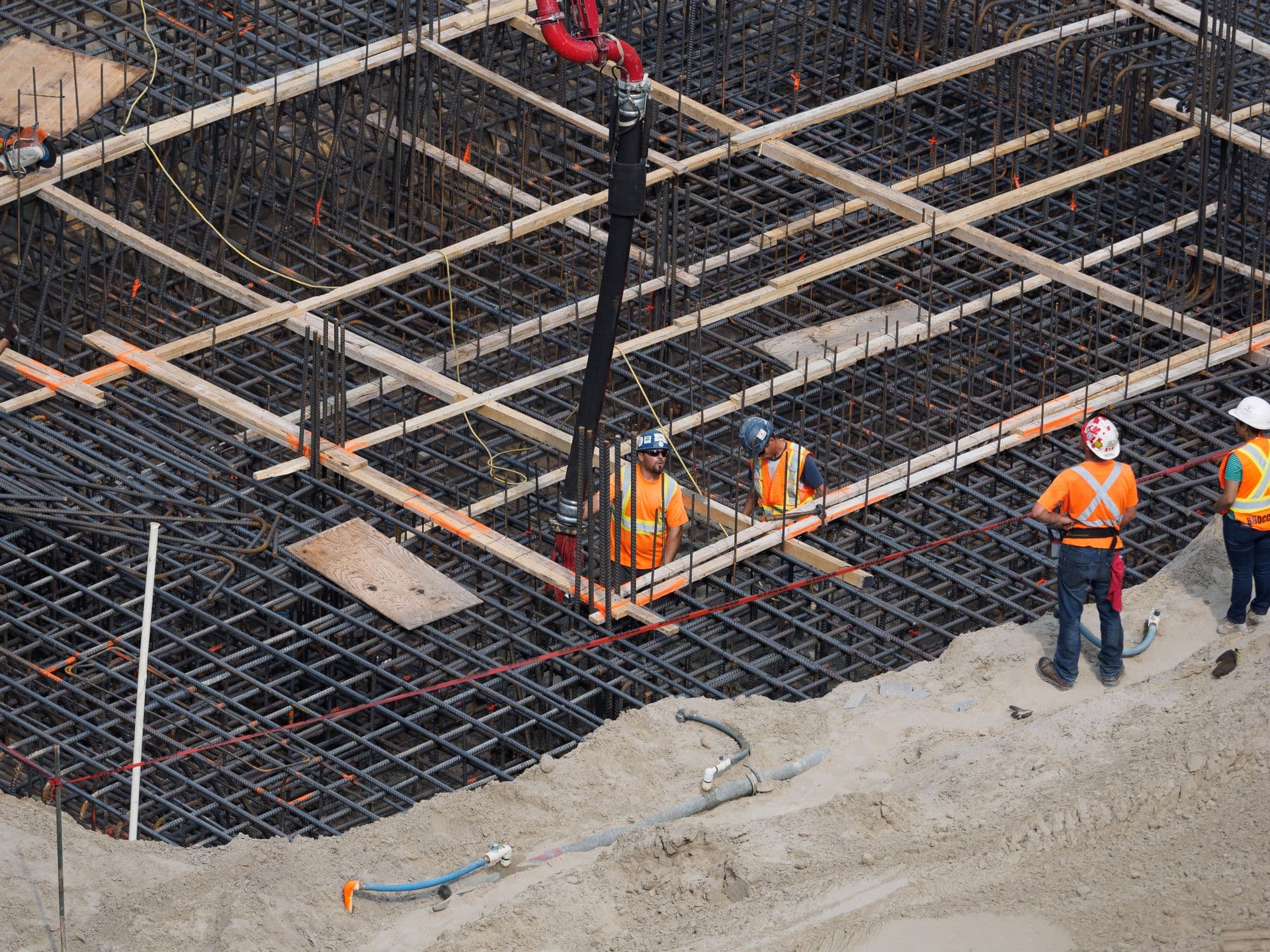Crew in hi-vis on a rebar mat with layout string lines across a foundation