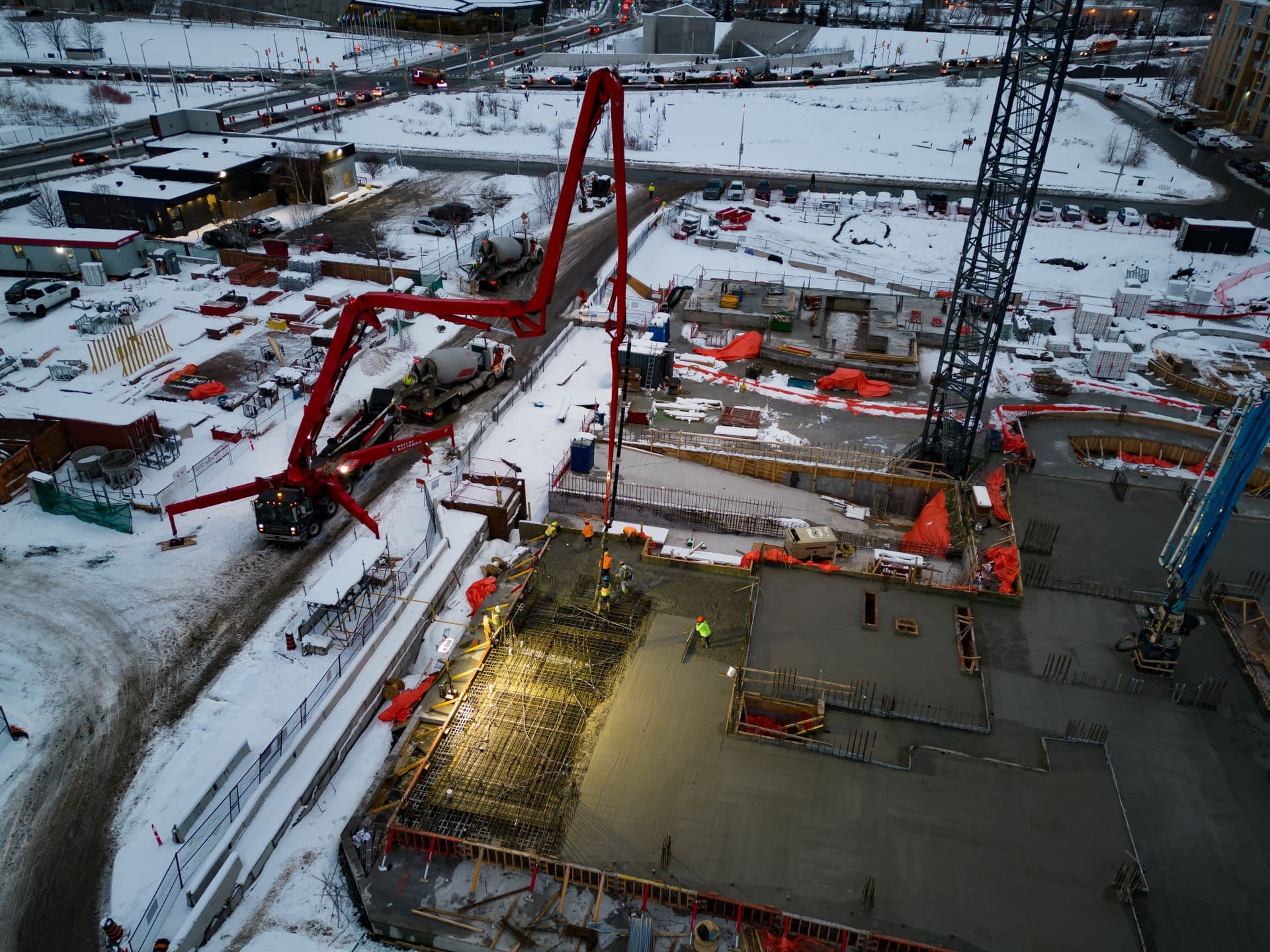 Aerial of a snow-covered construction site with a concrete pump boom over slab forms