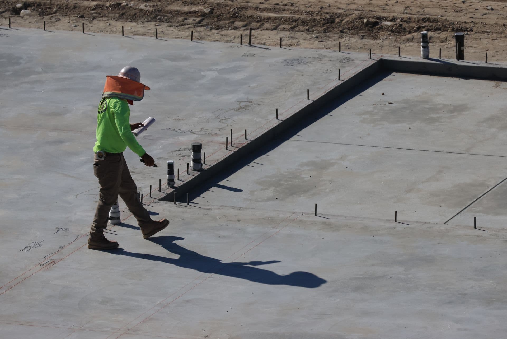 Worker crossing a fresh concrete slab marked out with layout lines
