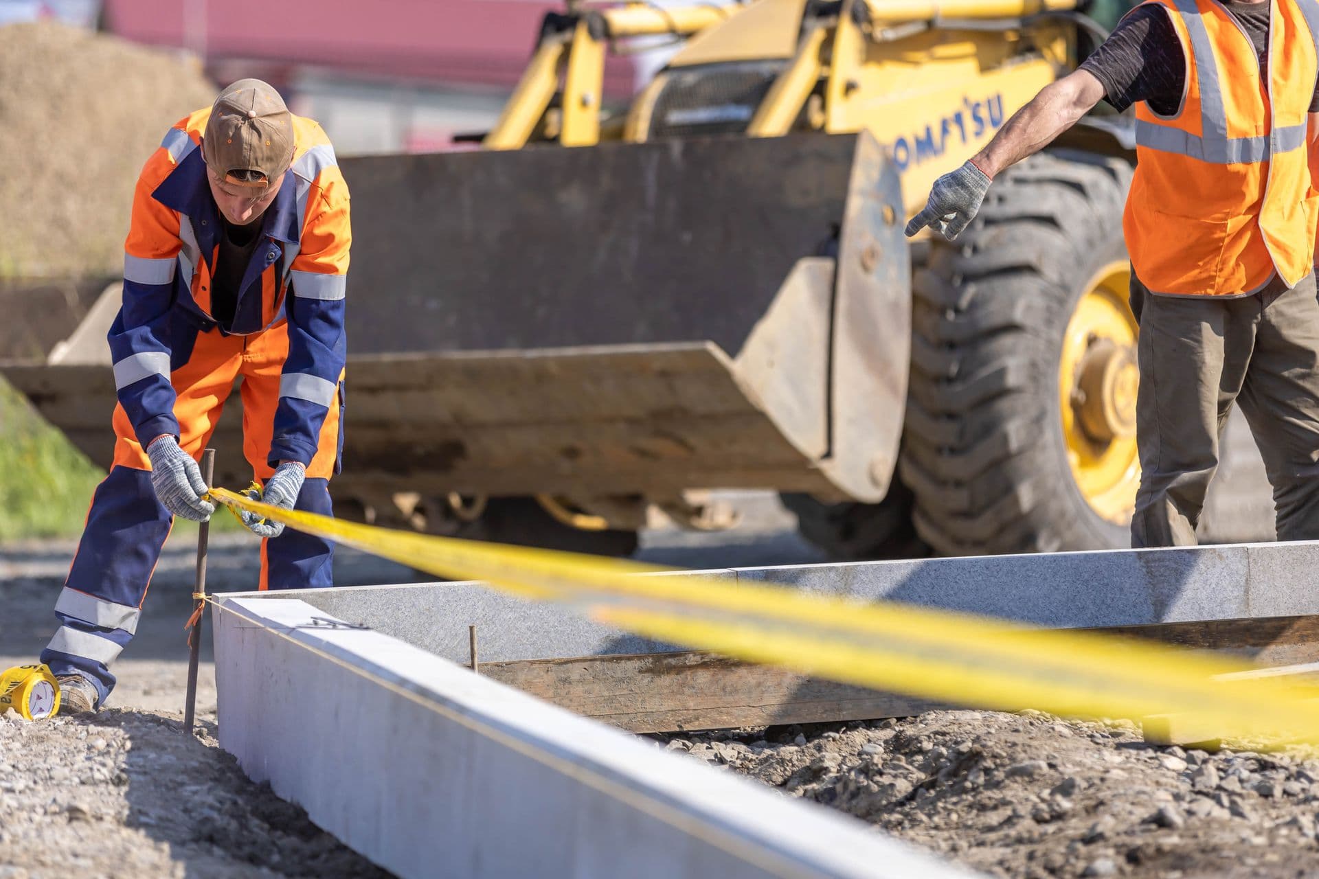 Two workers tape-checking a placed concrete element against the drawings